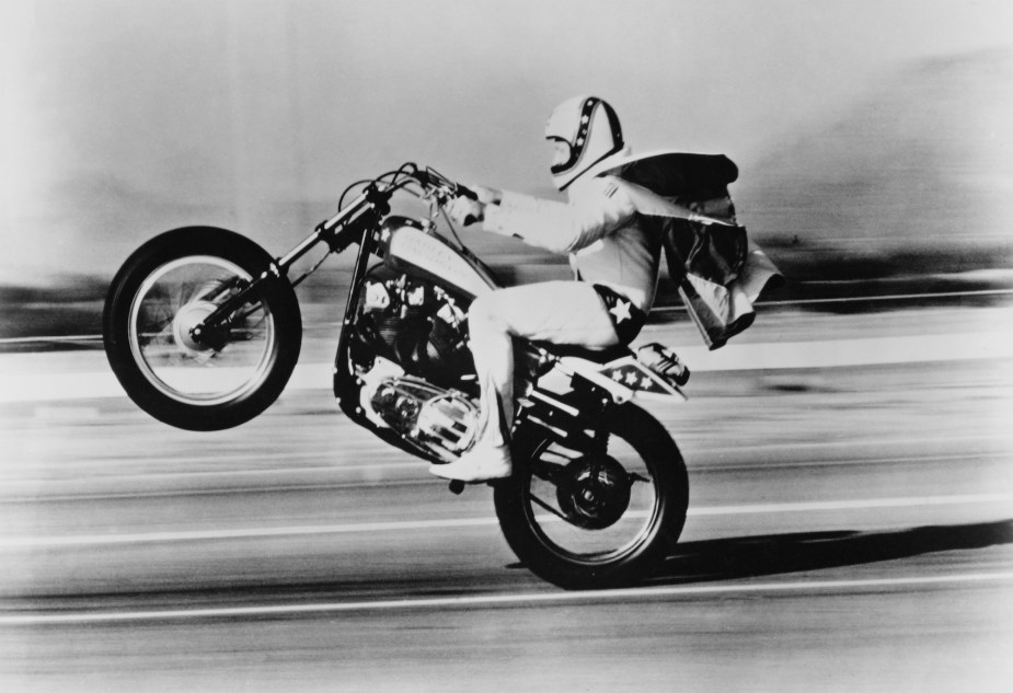 American stunt rider Evel Knievel (1938-2007) pops a wheelie on his Harley-Davidson motorcycle circa 1975