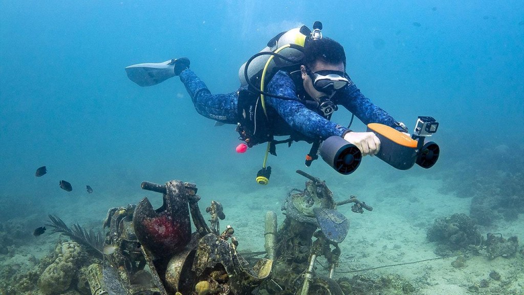 A diver underwater propelled by an orange Geneinno S2 water scooter with a GoPro camera.