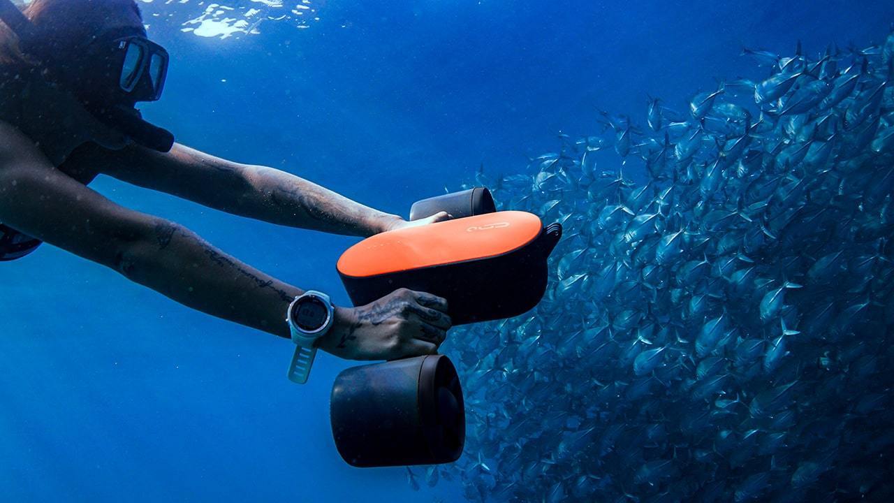 A diver underwater propelled by an orange Geneinno S2 water scooter.