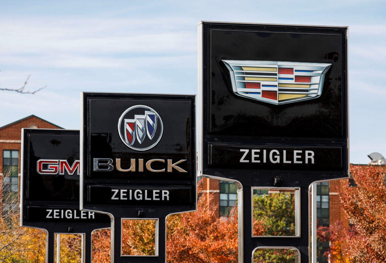 Signs outside of a General Motors car dealership advertise Cadillac, Buick, and GMC cars