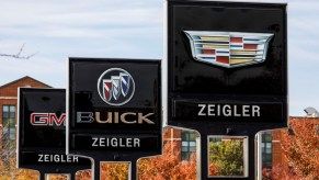 Signs outside of a General Motors car dealership advertise Cadillac, Buick, and GMC cars