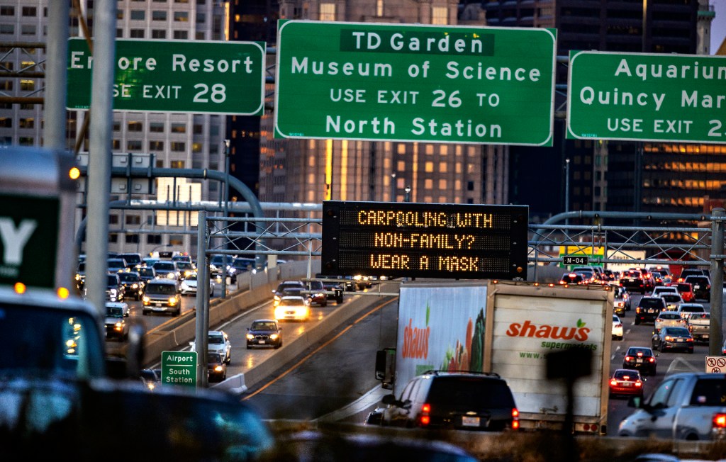 An image of several cars in traffic on a highway with a COVID-19 message on a large sign.