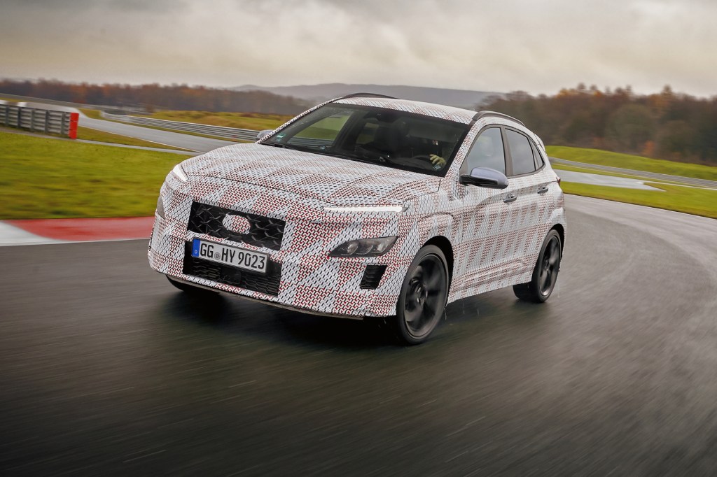 A camouflaged white Hyundai KONA N Prototype driving on a track