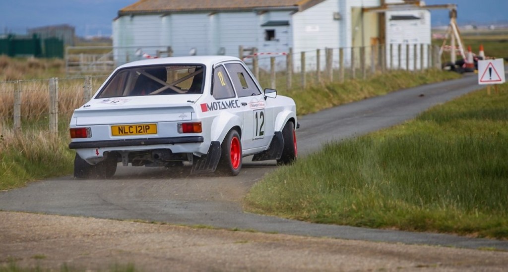 The rear view of a white MST Mk2 Ford Escort Group-4 Rally sliding around a corner