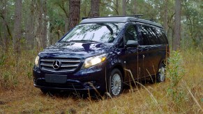 A navy-blue Mercedes-Benz Metris Getaway camper van parked in a wooded area