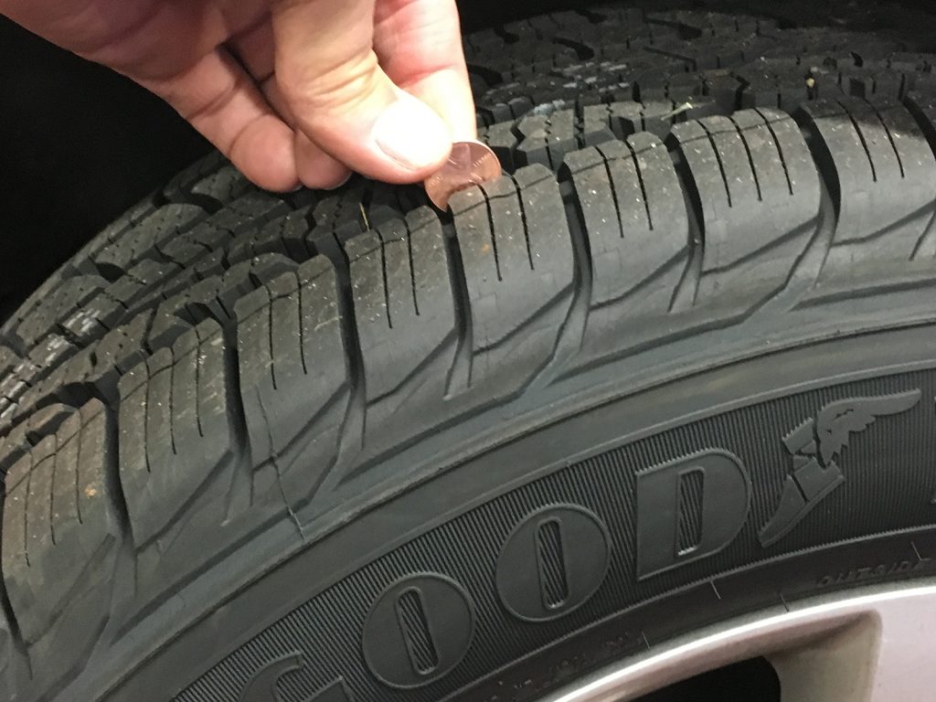 Someone performing the penny test by lowering a penny into a tire's grooves to measure the tread depth