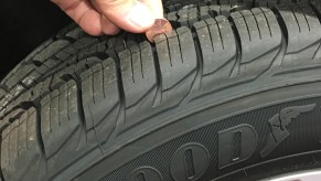 Someone performing the penny test by lowering a penny into a tire's grooves to measure the tread depth