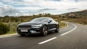 A dark-colored Polestar 1 travels on a two-lane road in the country