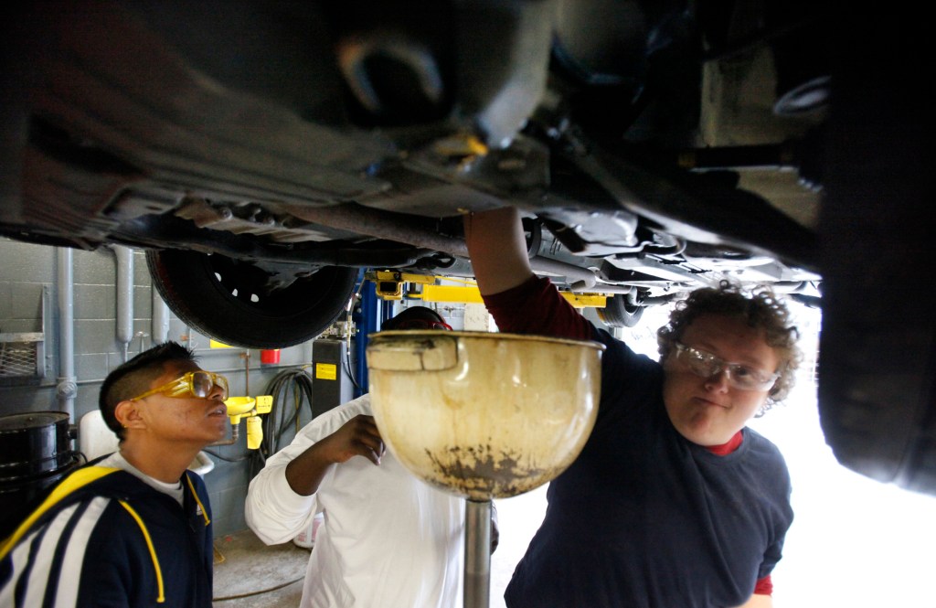 Two high school students change a car's engine oil