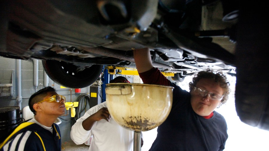 Two high school students change a car's engine oil