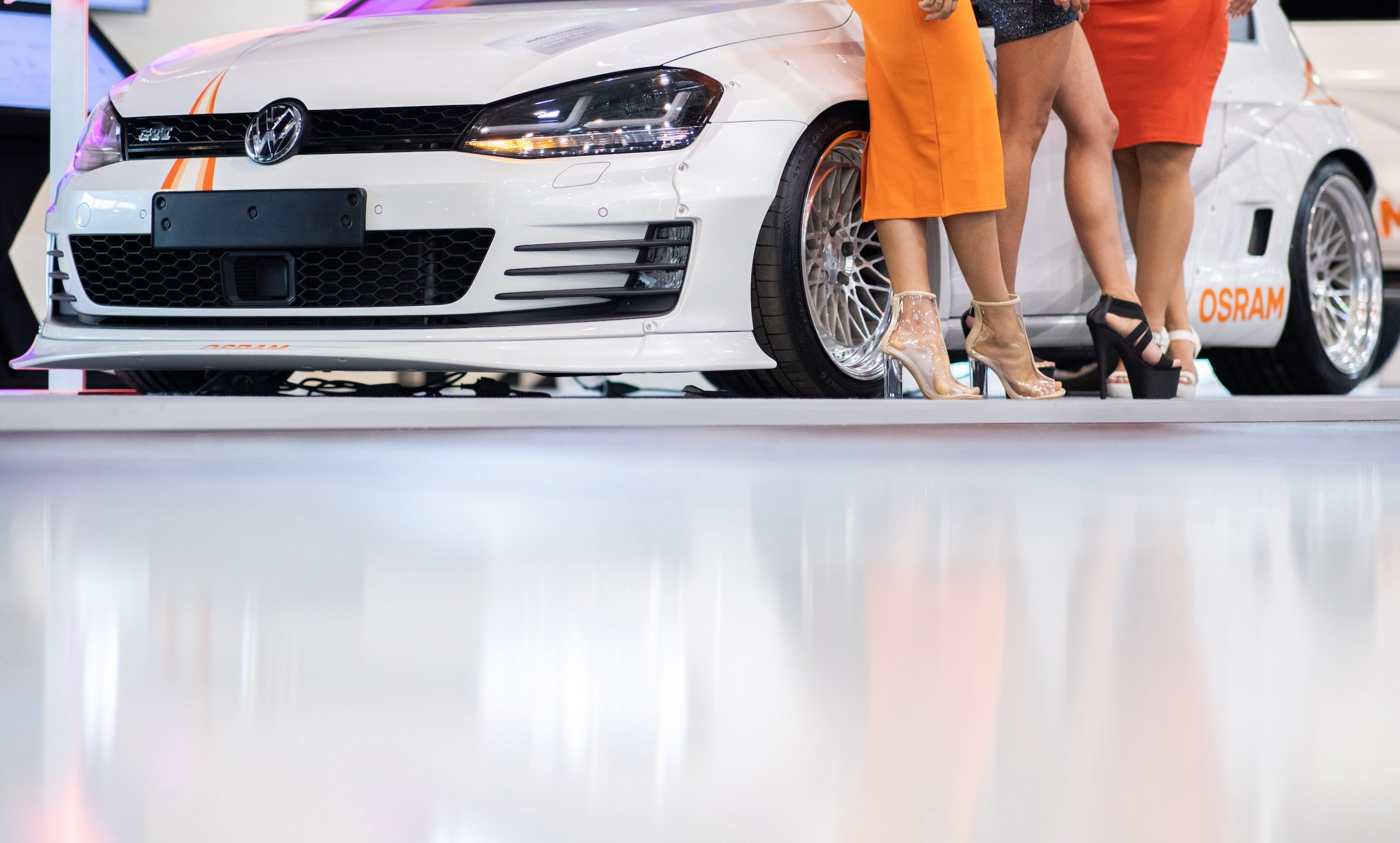 Women with high shoes posing at the Tuning Fair Essen Motor Show for visitors in front of a Golf GTI
