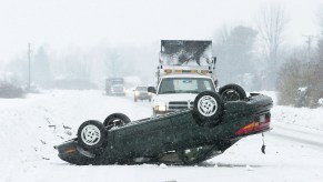 An overturned black car on a snow-covered highway