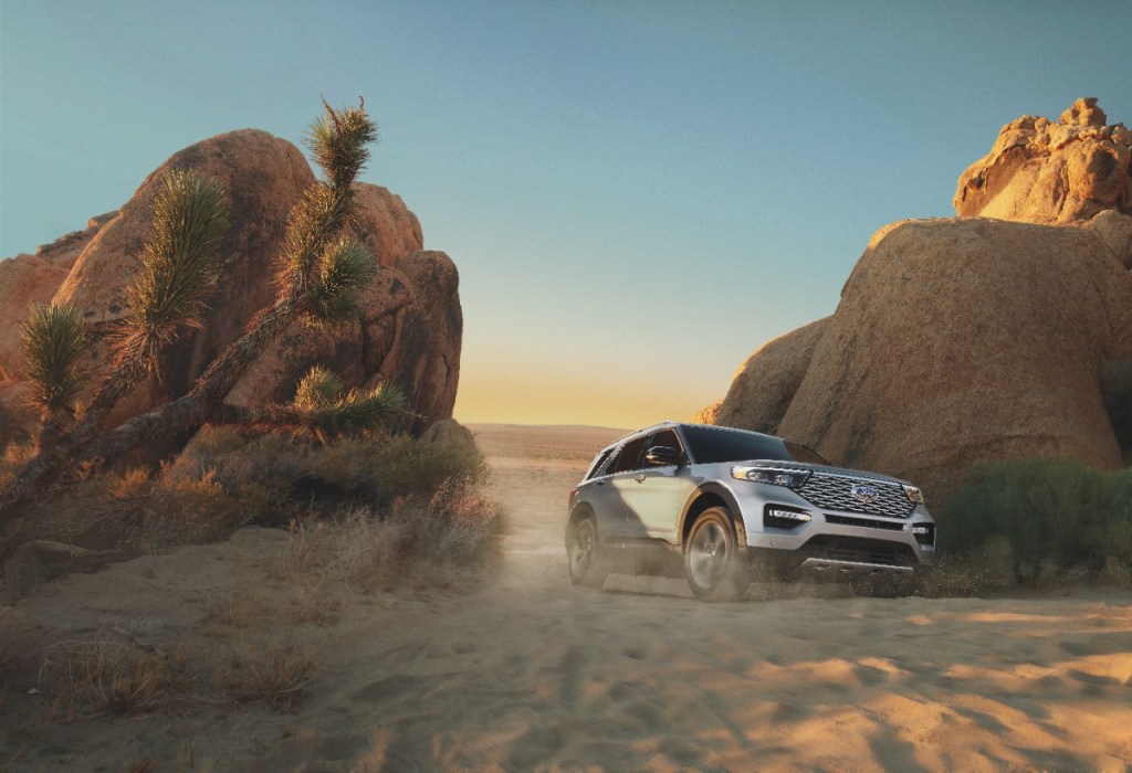 A silver 2021 Ford Explorer driving between two boulders on a sand pathway