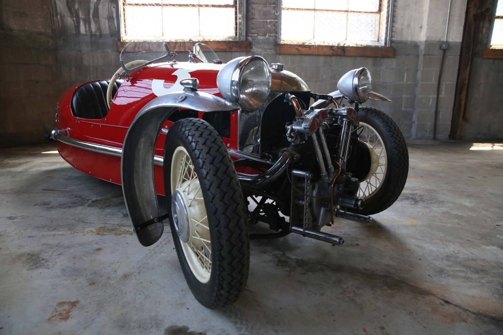 The front 3/4 view of a red 1933 Morgan 3-Wheeler Super Sport with a Matchless V-twin in a concrete garage