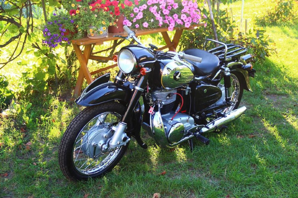 A black-and-silver 1956 Honda Dream MF350 on a lawn with some flowers