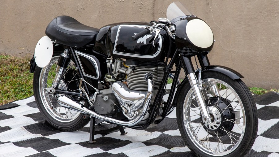 A black 1956 Matchless G45 production race motorcycle by a wall on a black-and-white checkerboard