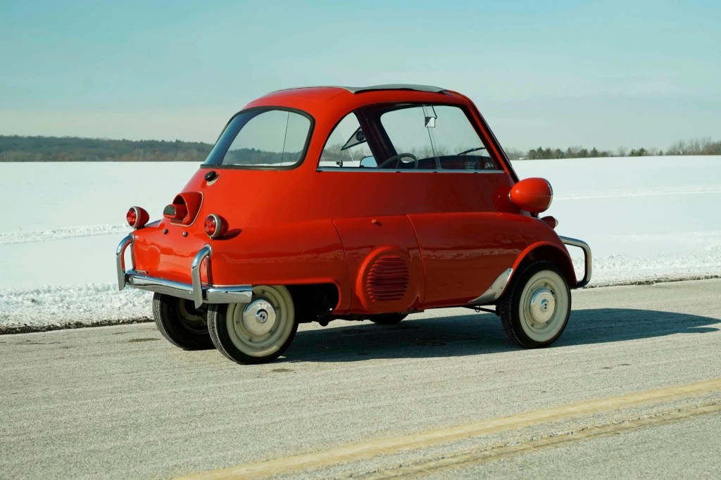 The rear 3/4 view of a red 1958 BMW Isetta 300 parked by a snow-covered field
