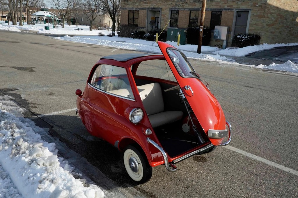 A red 1958 BMW Isetta 300 parked on a snowy city street with its door open