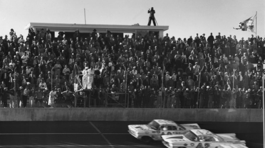 Three NASCAR cars, including Lee Petty's No. 42 Oldsmobile Super 88, head toward the finish line at the first Daytona 500 in 1959