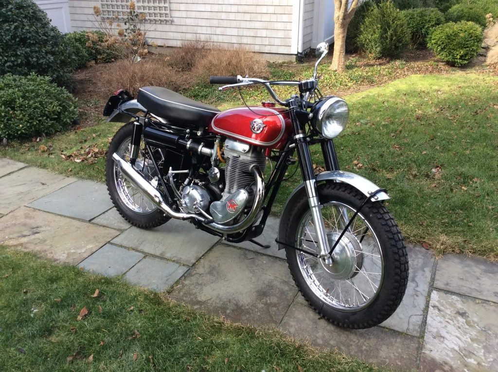 A red-silver-and-black 1961 Matchless G80CS parked on a stone path on a lawn