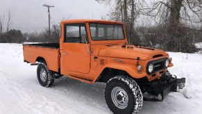The front 3/4 view of an orange 1964 FJ45 Toyota Land Cruiser pickup in the snow