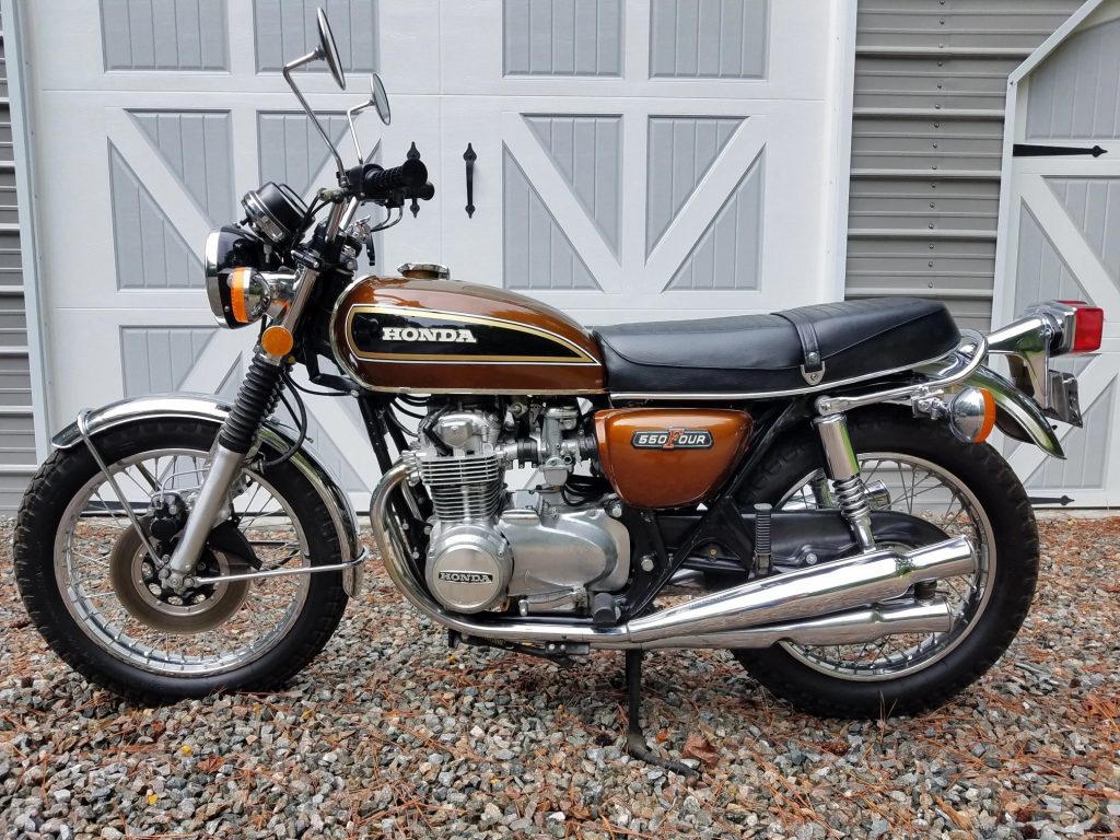The side view of a gold-brown 1976 Honda CB550 Four in front of a white shed