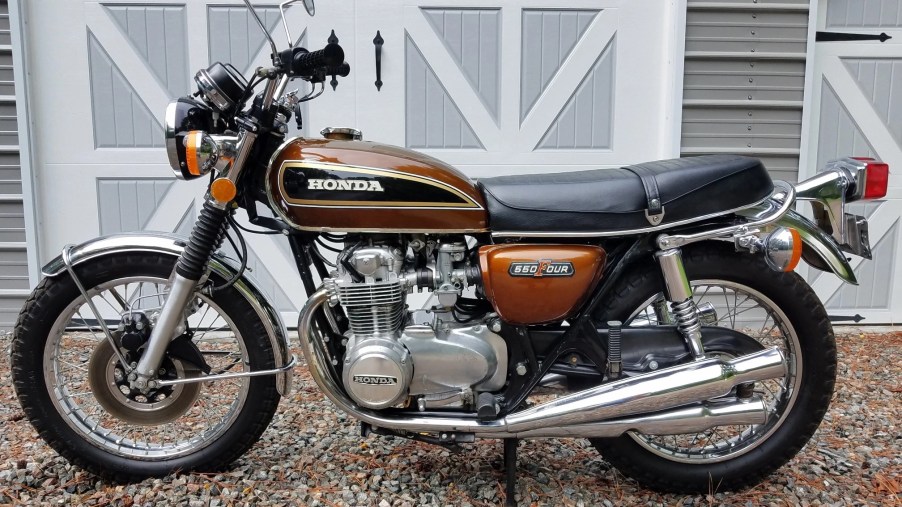 The side view of a gold-brown 1976 Honda CB550 Four in front of a white shed