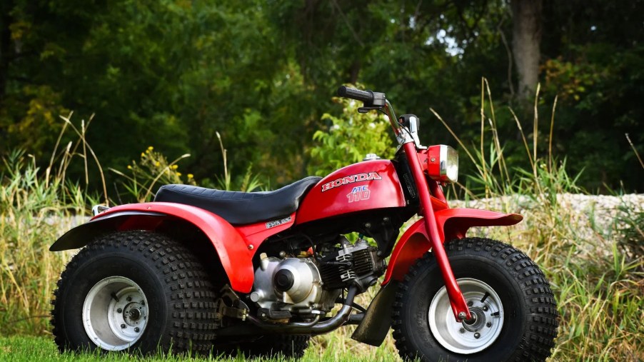 The side view of a red 3-wheeled 1979 Honda ATC 110 in a field