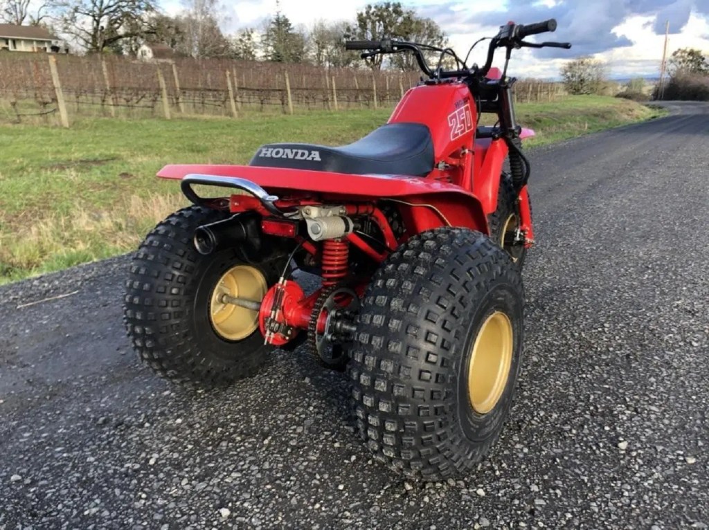 The rear 3/4 view of a red 1981 Honda ATC 250R on a gravel road
