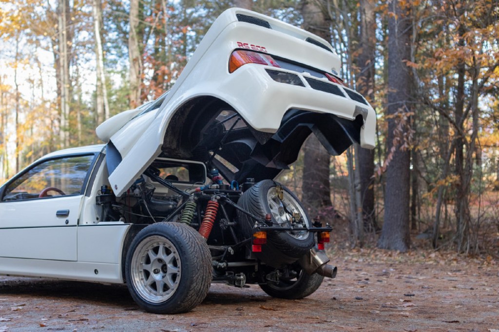 The rear of a white 1986 Ford RS200 Evolution in the forest with its rear winged section raised showing its chassis and engine