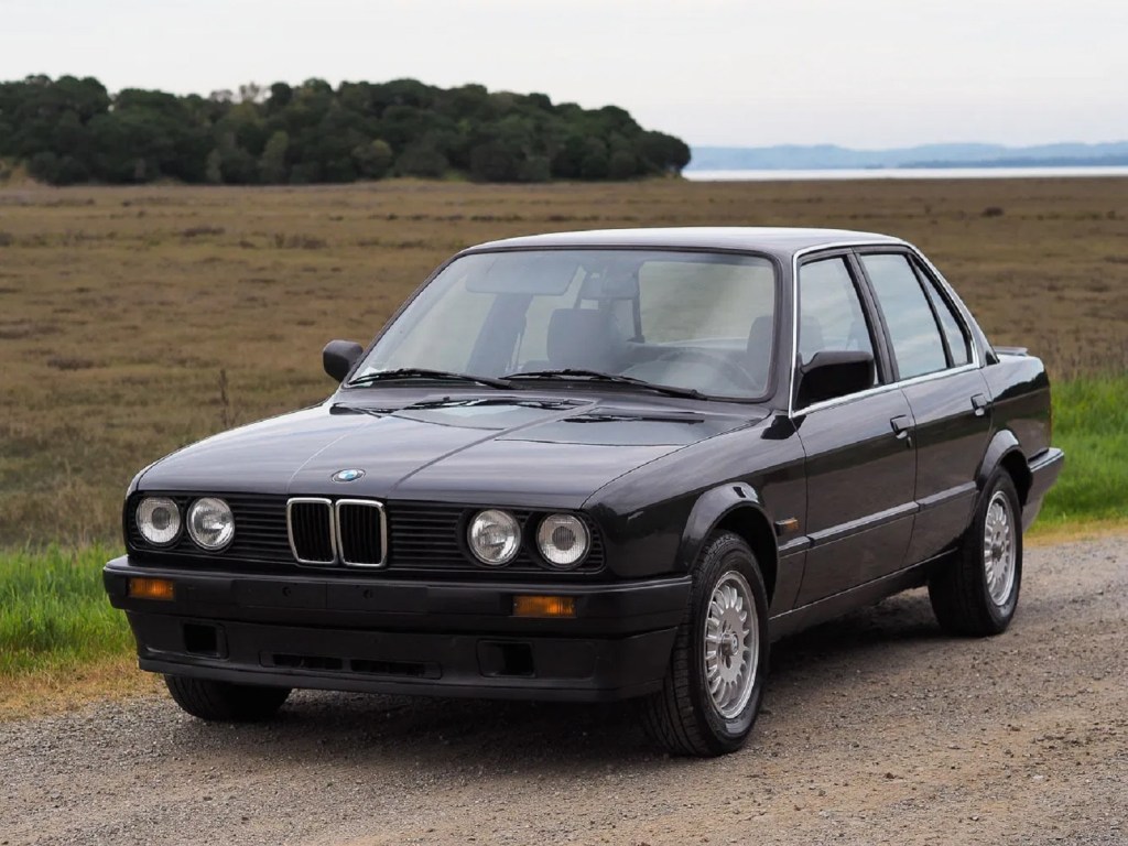 A black 1988 BMW 320is by a field