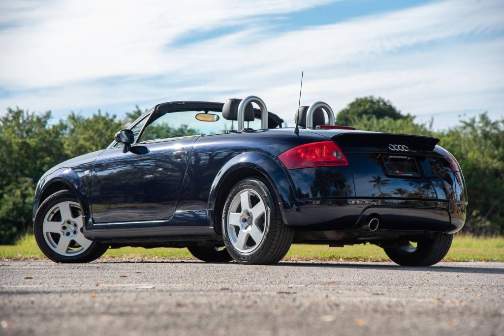 A low-angle rear 3/4 view of a black 2002 Audi TT Roadster with its top down and radio antenna up