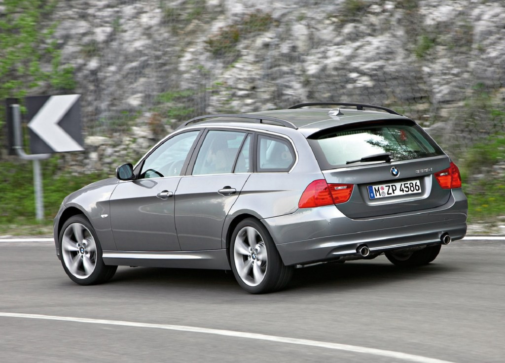 The rear 3/4 view of a gray 2009 E91 BMW 335d Wagon driving around a mountain road corner