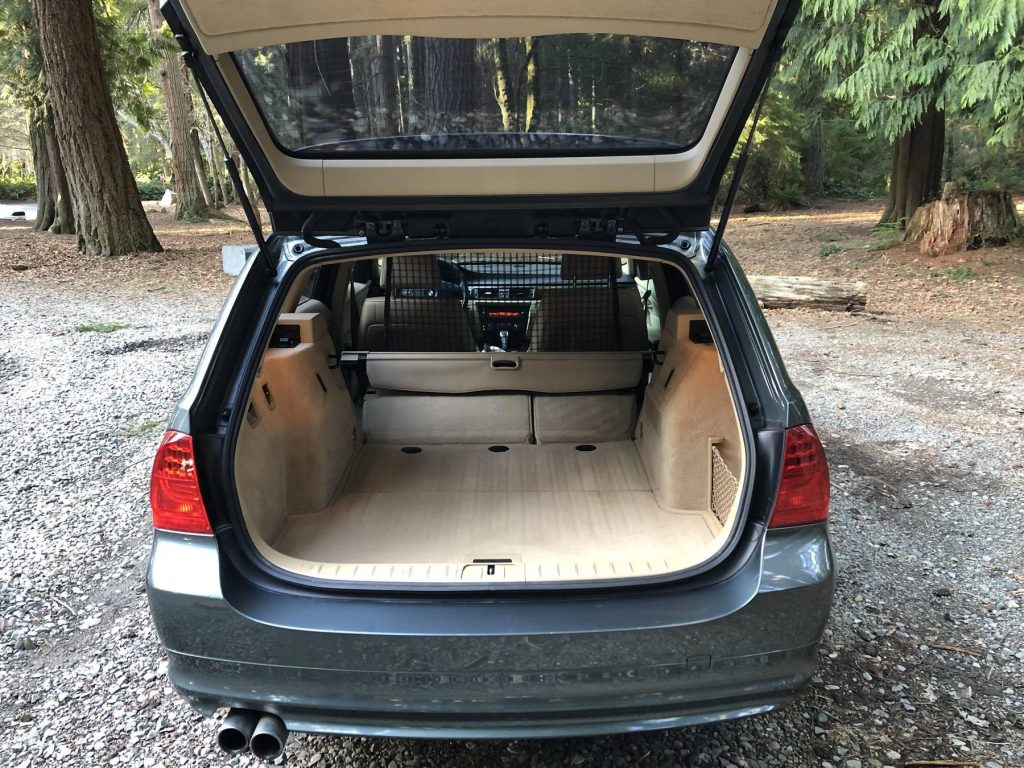 The rear view of a dark-green 2011 BMW 328i Sports Wagon's beige-leather interior with its rear seats folded