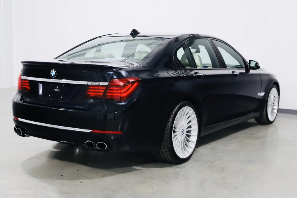 The rear 3/4 view of a dark-blue 2013 BMW Alpina B7 xDrive in a white warehouse