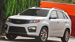 A white 2013 Kia Sorento parked near foliage and an orange building
