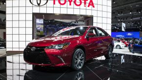 A red 2015 Toyota Camry on display at an auto show with Toyota in bold letters on the wall behind it.