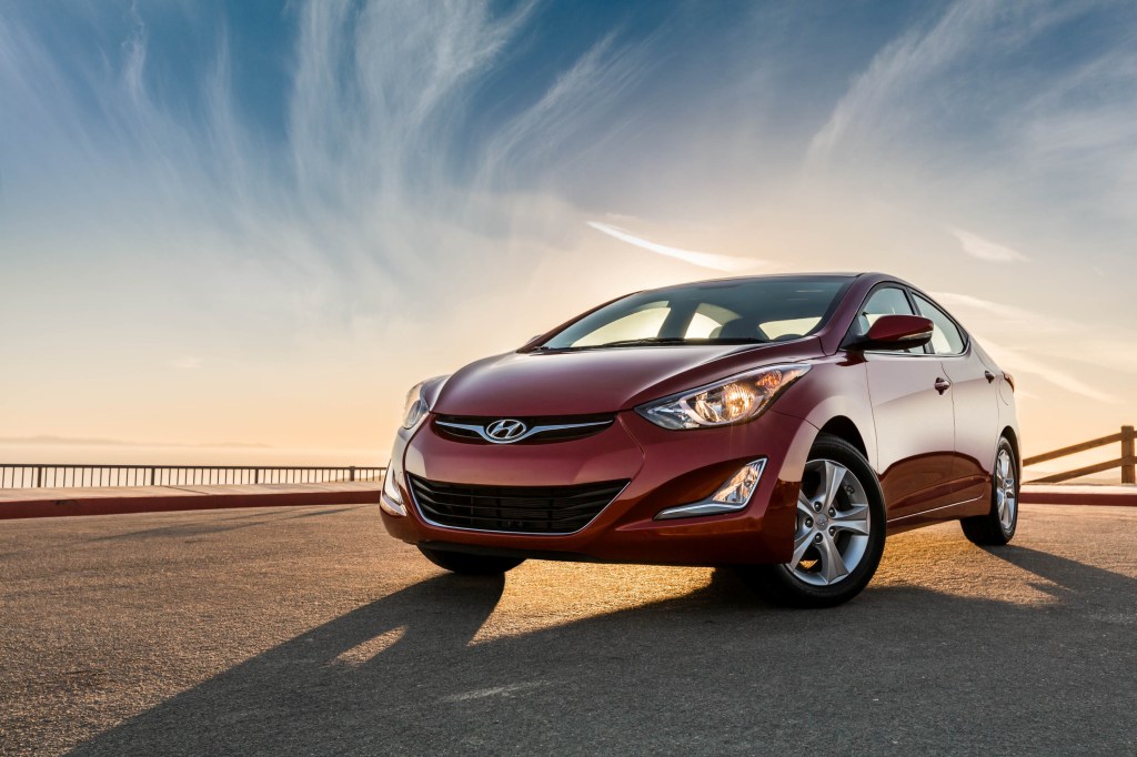 A red 2016 Hyundai Elantra on display in front of a colorful sky