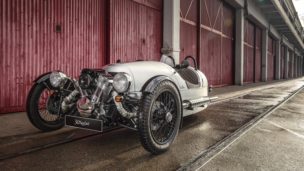 The front 3/4 view of a silver 2018 Morgan 3-Wheeler in front of a red barn