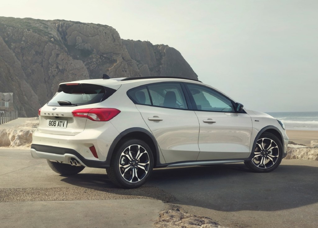 The rear 3/4 view of a white 2019 Ford Focus Active on a cliff-lined beach