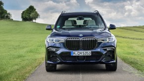 A dark-blue 2020 BMW X7 full-size crossover SUV parked on a narrow road passing through grassy hills