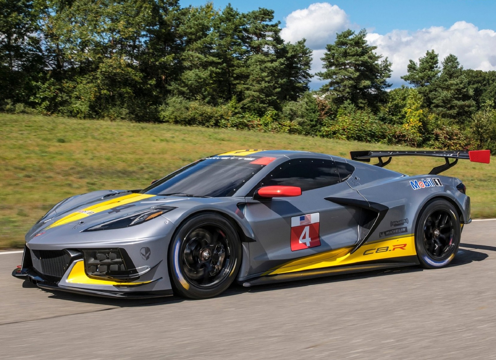 The gray-and-yellow 2020 Chevrolet Corvette C8.R drives down a forest-lined road