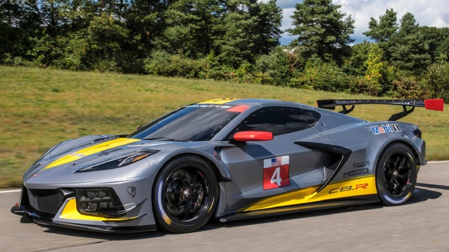 The gray-and-yellow 2020 Chevrolet Corvette C8.R drives down a forest-lined road
