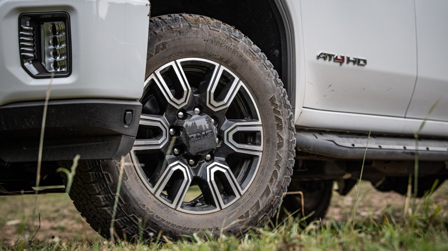 The driver's side door, tire, and front bumper of a white 2020 GMC Sierra HD AT4 pickup truck parked in the grass