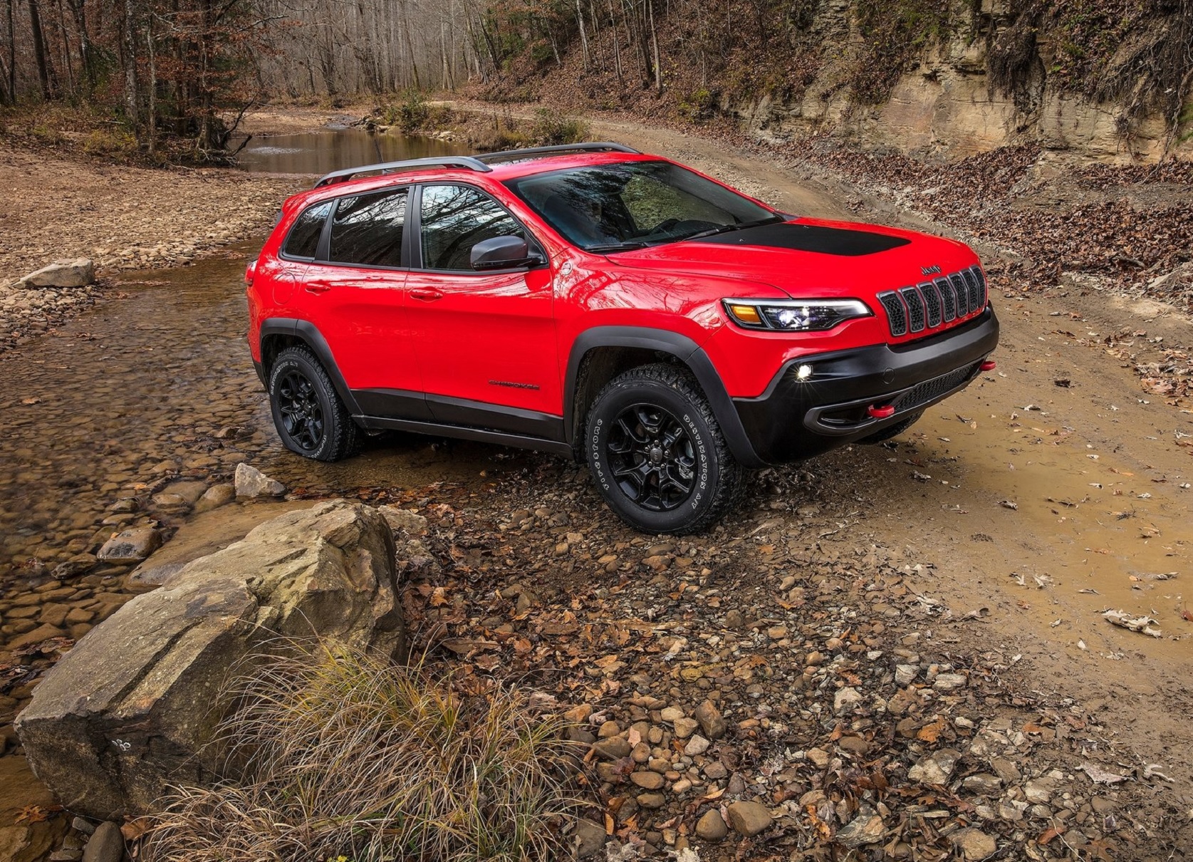 A red-and-black 2020 Jeep Cherokee Trailhawk on a muddy off-road trail
