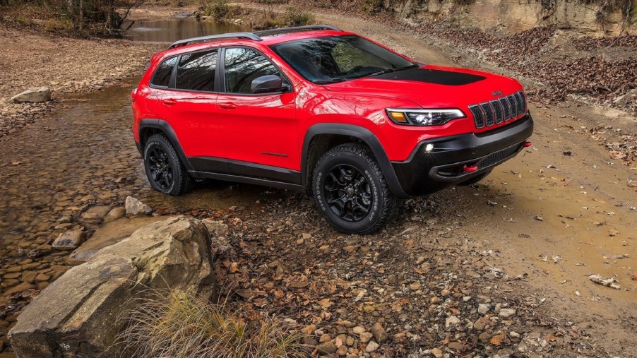 A red-and-black 2020 Jeep Cherokee Trailhawk on a muddy off-road trail