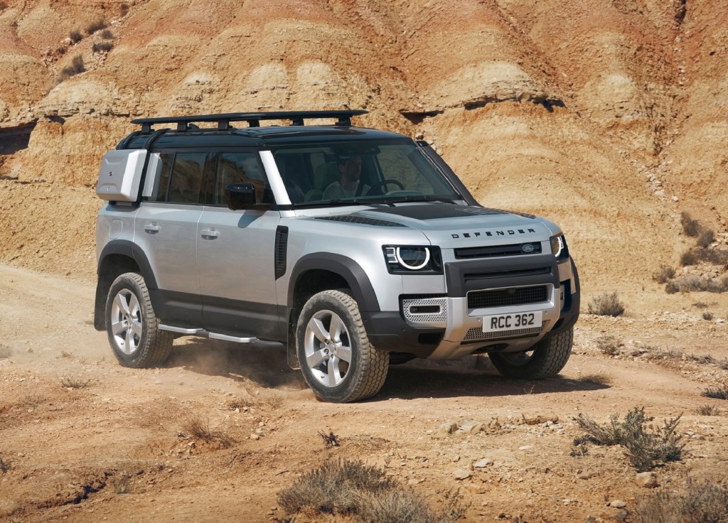 A silver 2020 Land Rover Defender 110 with exterior-mounted cases and a roof rack in the desert