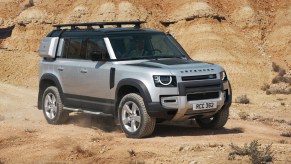 A silver 2020 Land Rover Defender 110 with exterior-mounted cases and a roof rack in the desert