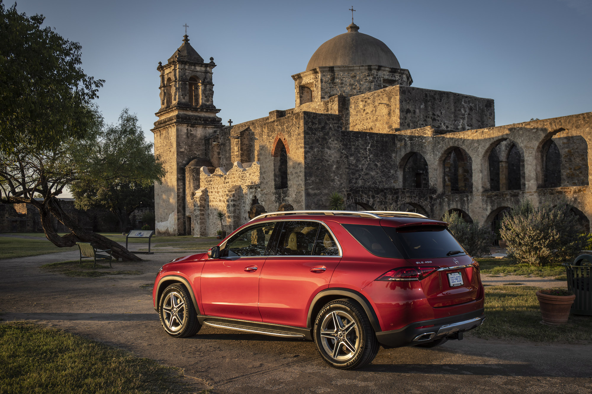 A red 2020 Mercedes-Benz GLE450 4MATIC compact luxury SUV parked outside the historic San José y San Miguel de Aguayo in San Antonio, Texas