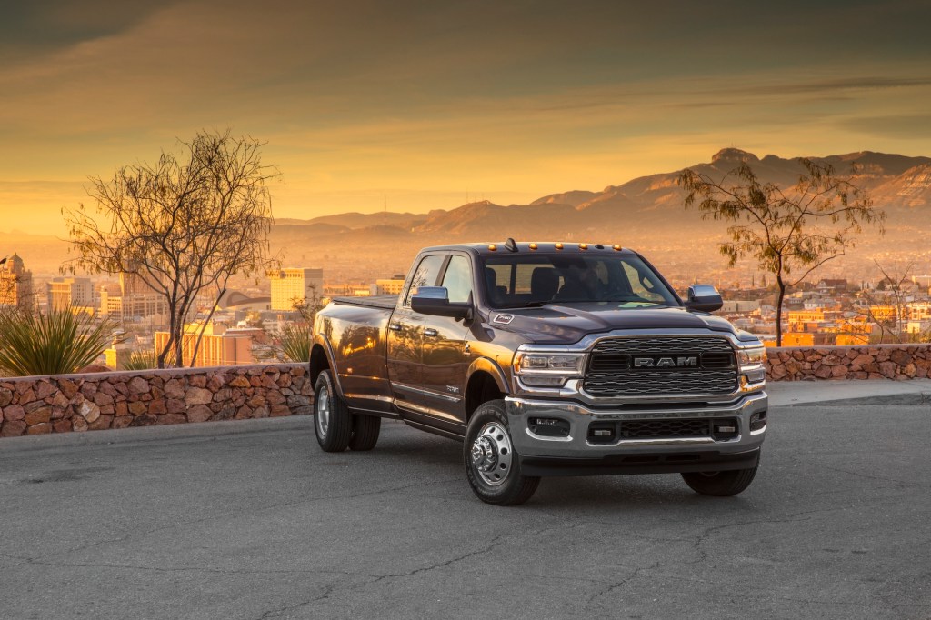 A dark 2020 Ram 3500 Heavy Duty Limited Crew Cab Dually pickup truck with a cityscape, mountains, and sunset in the background